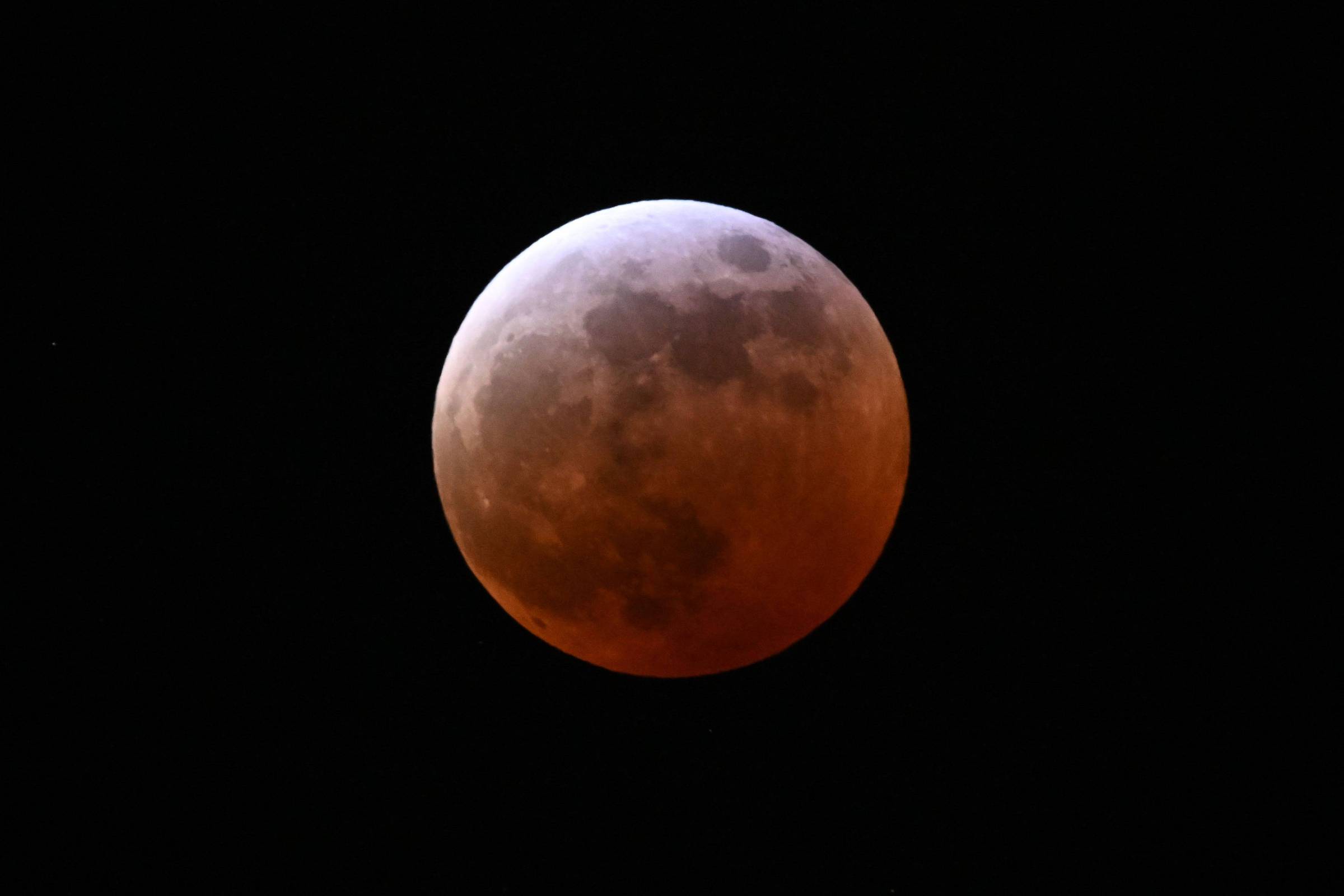 A imagem mostra a Lua durante um eclipse, com uma parte iluminada e outra parte em tons avermelhados, contra um fundo negro.
