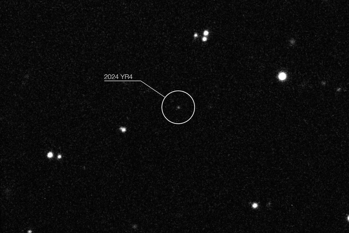 A imagem mostra um fundo escuro com várias estrelas visíveis. No centro, há um círculo branco destacando o asteroide identificado como 2024 YR4, que é um ponto luminoso entre as estrelas. O nome do asteroide está indicado com uma linha apontando para ele.