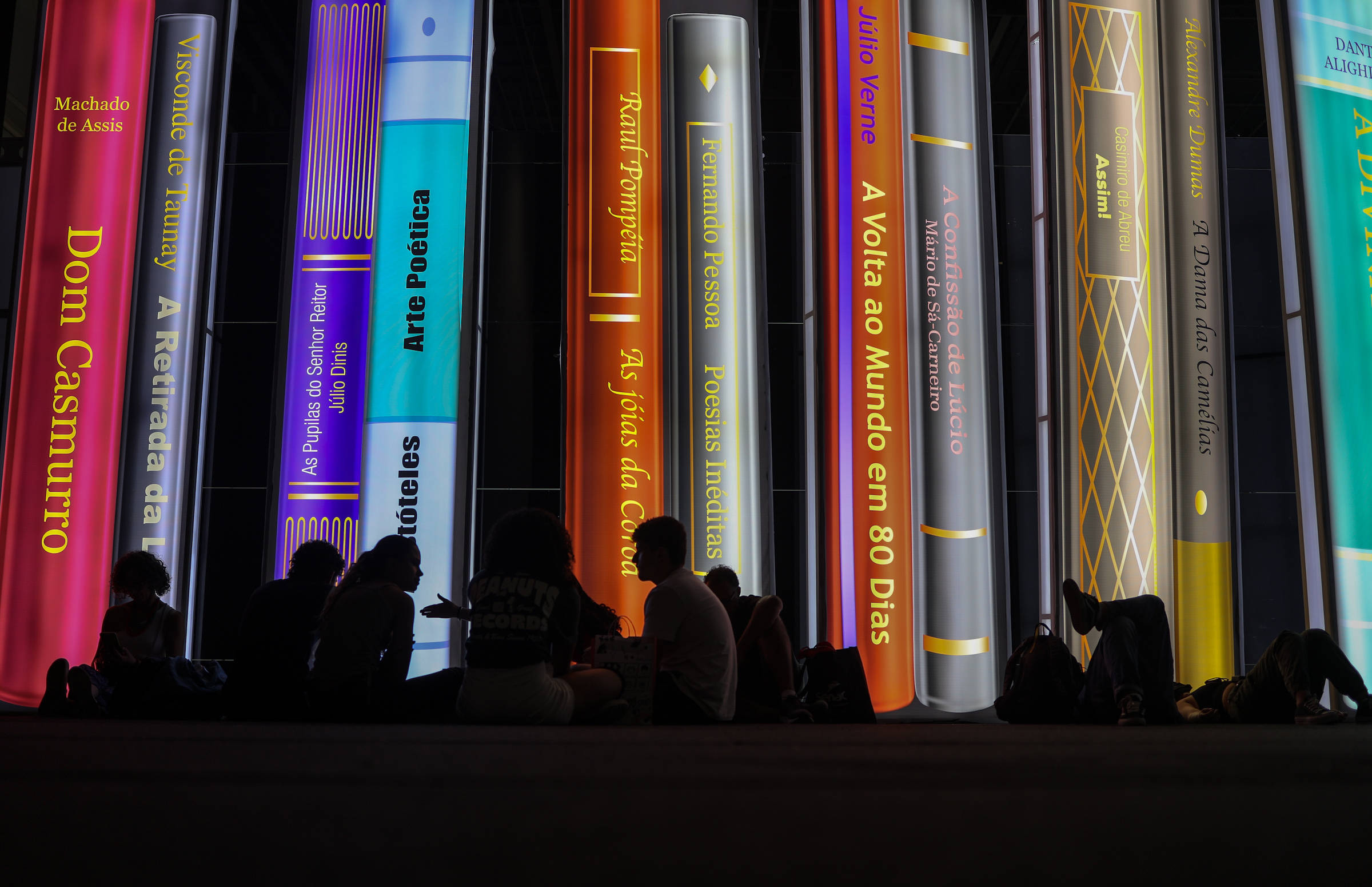 sombras de pessoas contra imagens de lombadas de livros gigantes