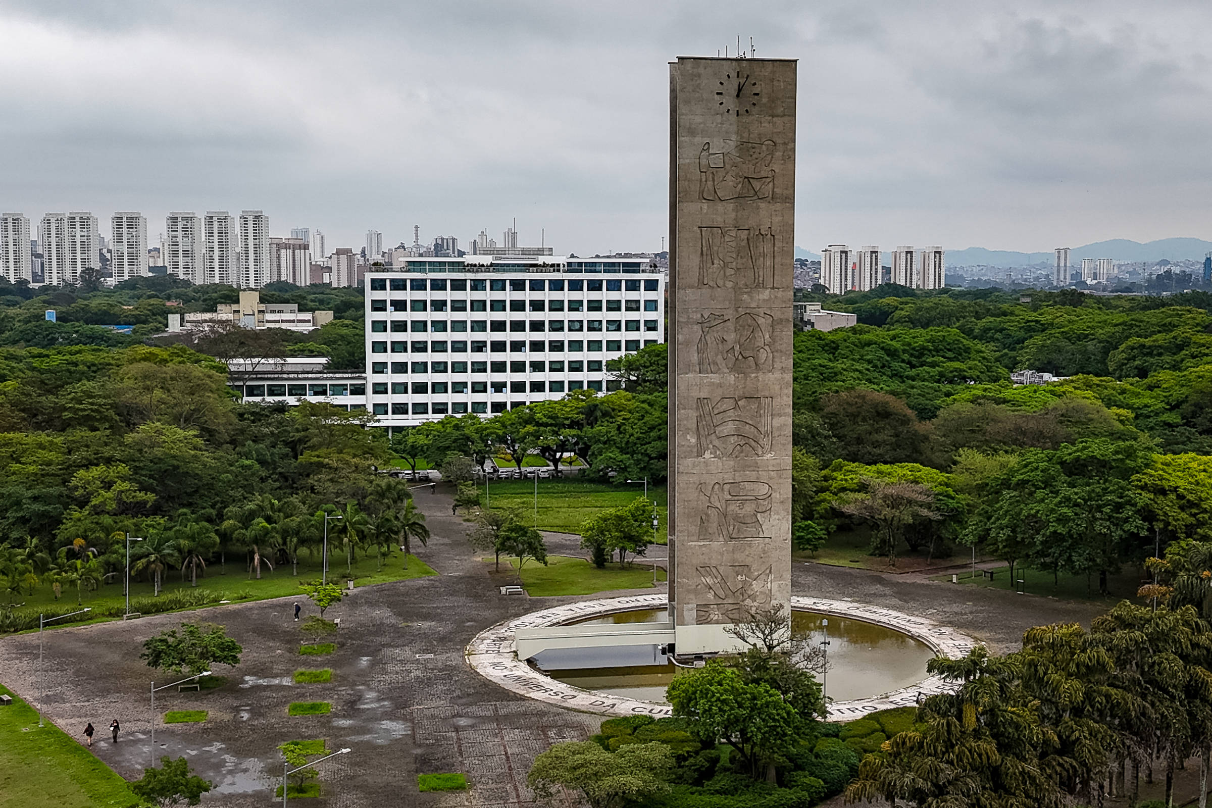 Torre do Relógio com painéis de arte em relevo no centro de uma praça circular com espelho d