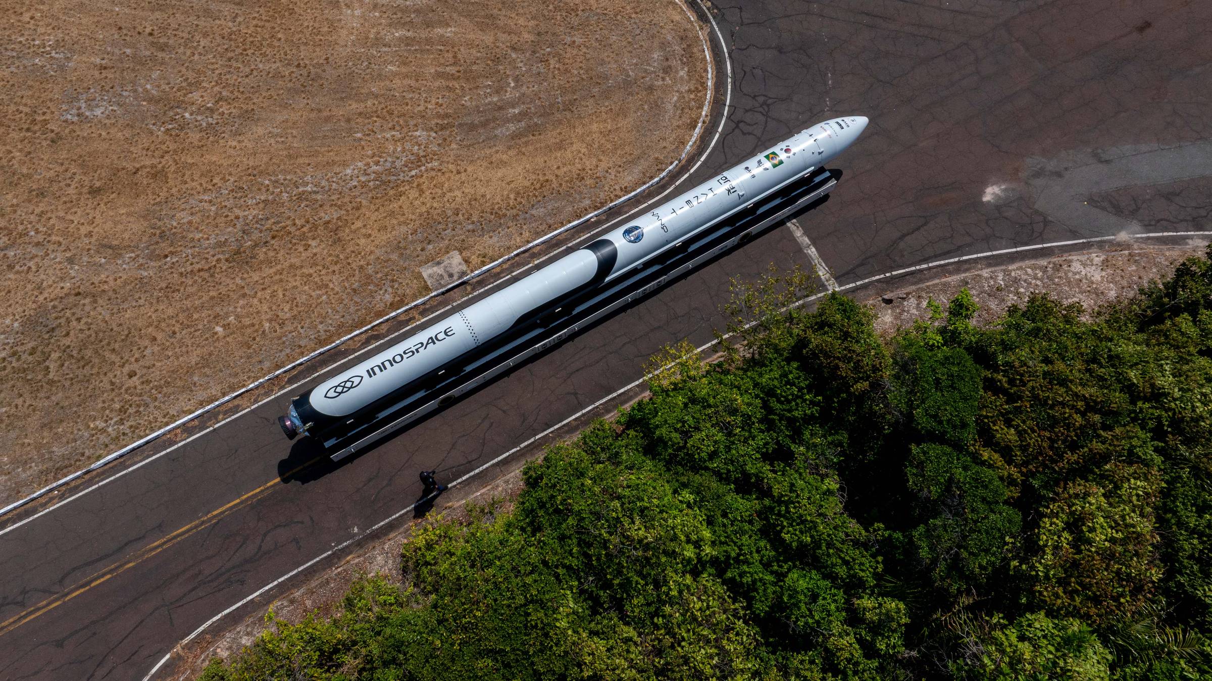 Foguete GSLV Mk III da ISRO posicionado em pista de lançamento, visto de cima. Vegetação densa ao lado da pista e área seca ao redor.