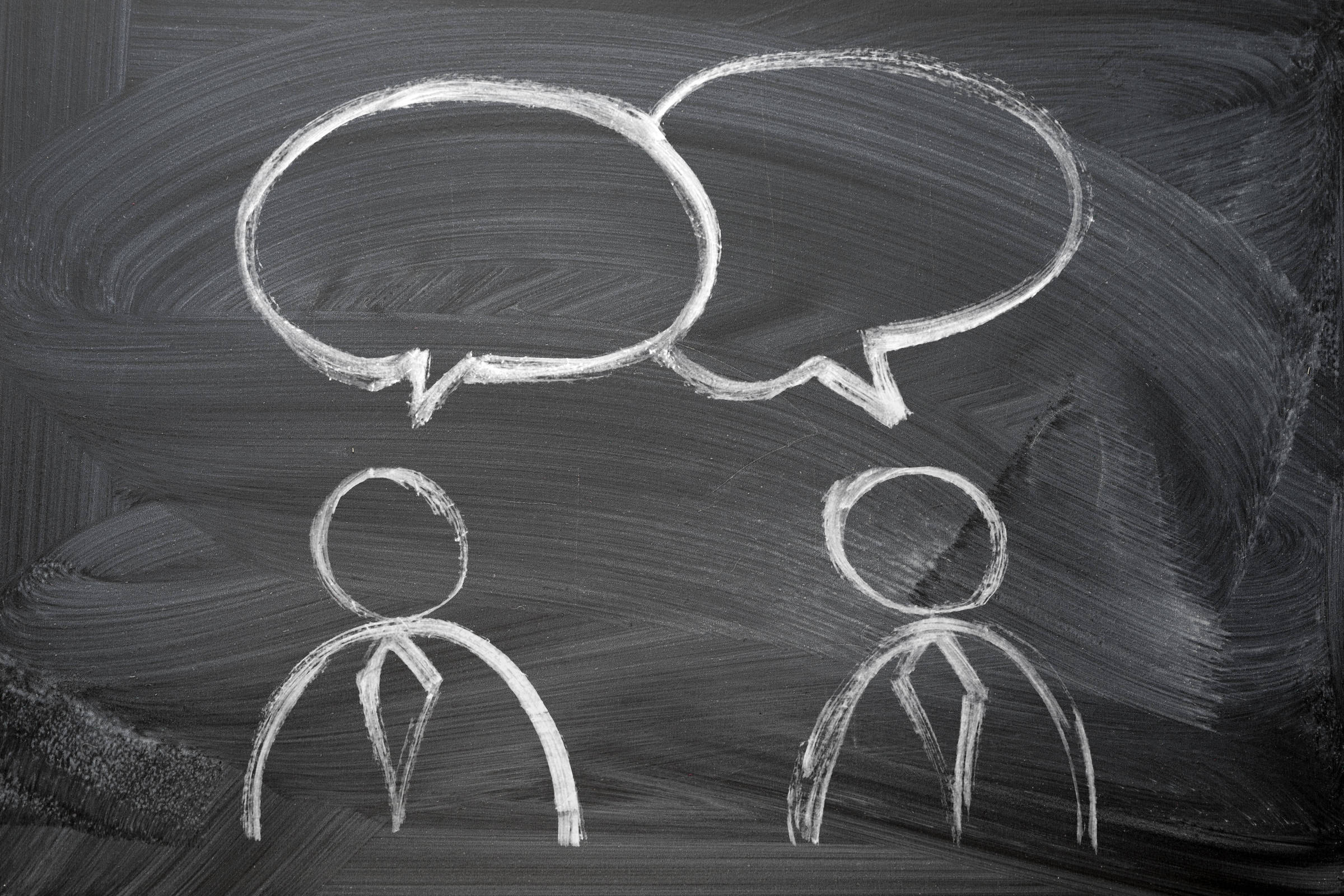 Desenho a giz branco em quadro negro mostra duas figuras humanas estilizadas com gravatas, cada uma com um balão de fala acima da cabeça, indicando diálogo.