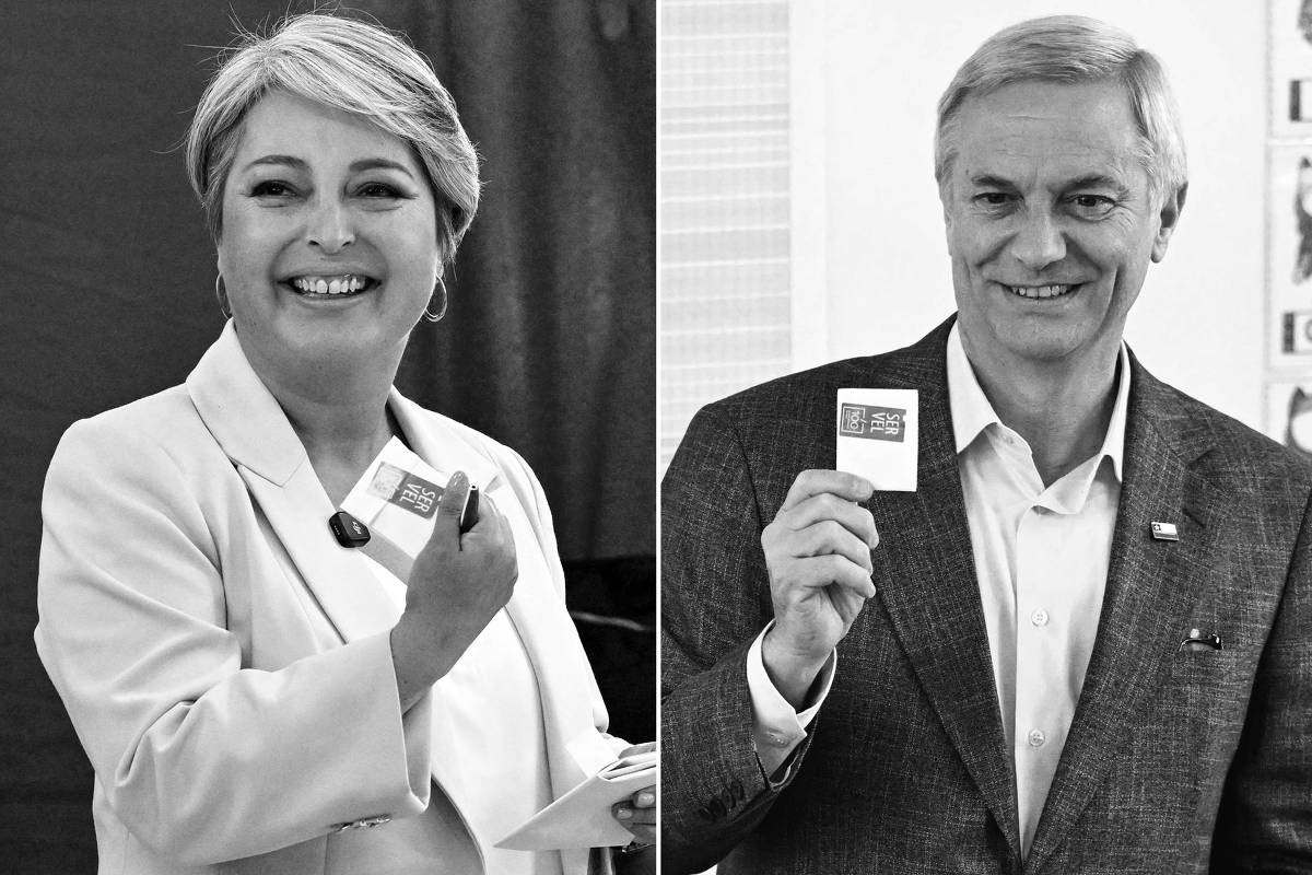 À esquerda, mulher de cabelo curto grisalho, vestindo blazer rosa claro e blusa branca, sorri segurando um cartão verde e branco. À direita, homem de cabelo grisalho, usando terno cinza e camisa azul clara, sorri segurando cartão semelhante. Fundo com cortina azul e gráficos.