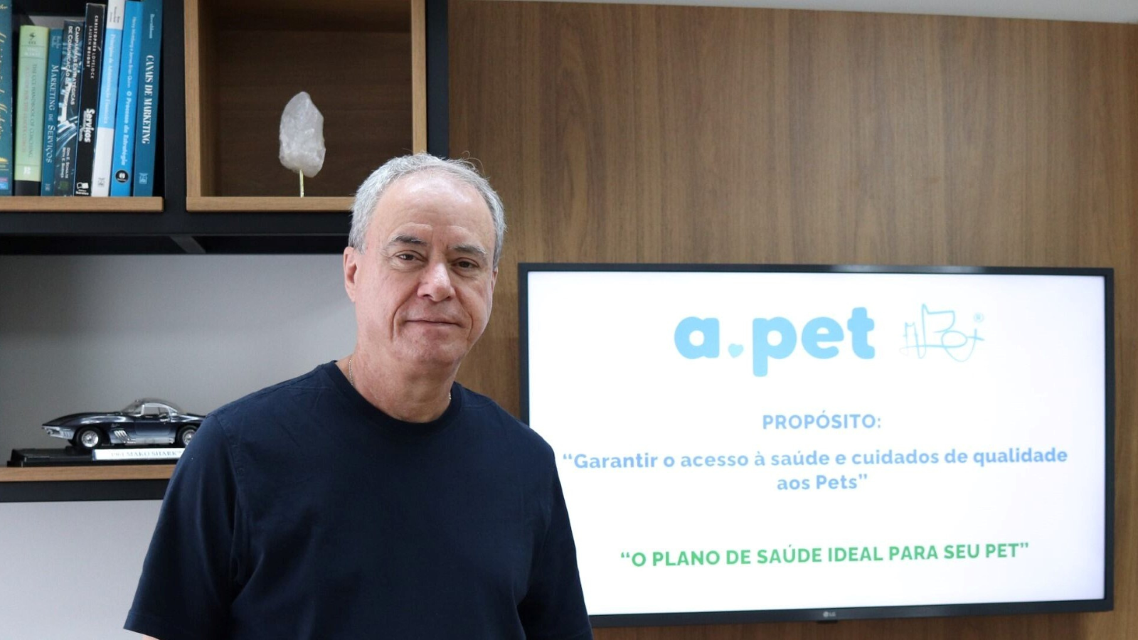 Luiz Gênova, CEO da APet, em ambiente corporativo, com painel institucional da empresa ao fundo destacando o propósito de garantir saúde de qualidade aos pets