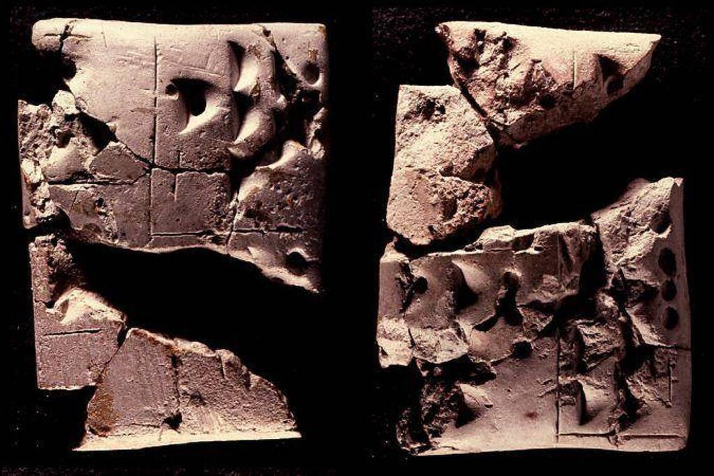 Dois fragmentos de tablete de argila com inscrições cuneiformes visíveis, exibindo marcas e rachaduras, sobre fundo preto.