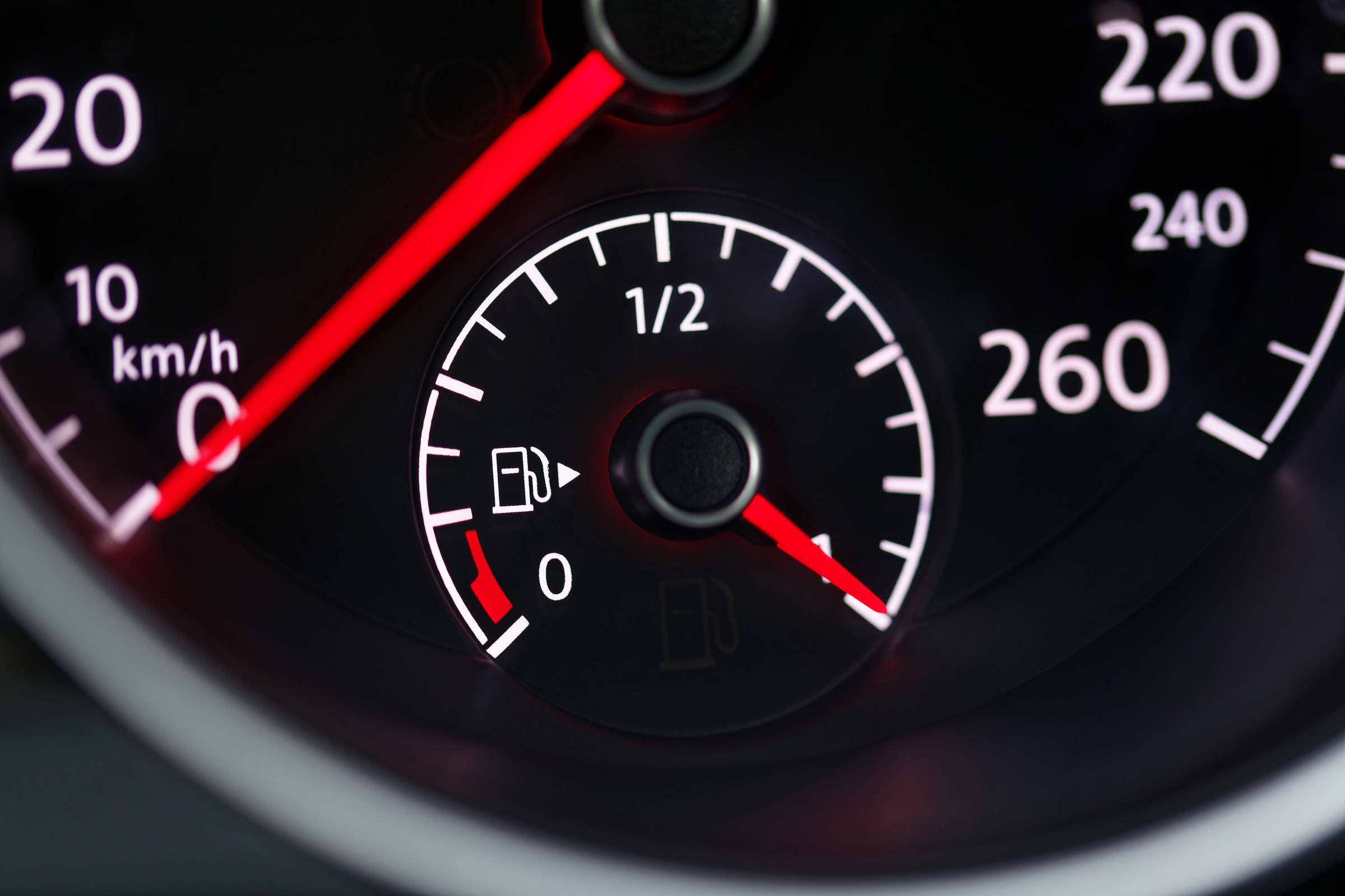 Mostrador do painel de um carro com o ponteiro do medidor de combustível apontando para próximo de zero, indicando tanque quase vazio. Ao redor, parte do velocímetro com marcações até 260 km/h.