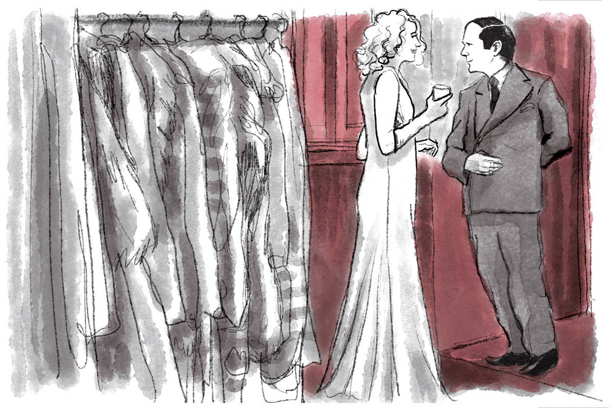 Cena do filme Blue Moon em que o protagonista, de terno, conversa enternecido com uma mulher alta, de vestido e loira. O casal está dentro de um closet cheio de casacos pendurados.