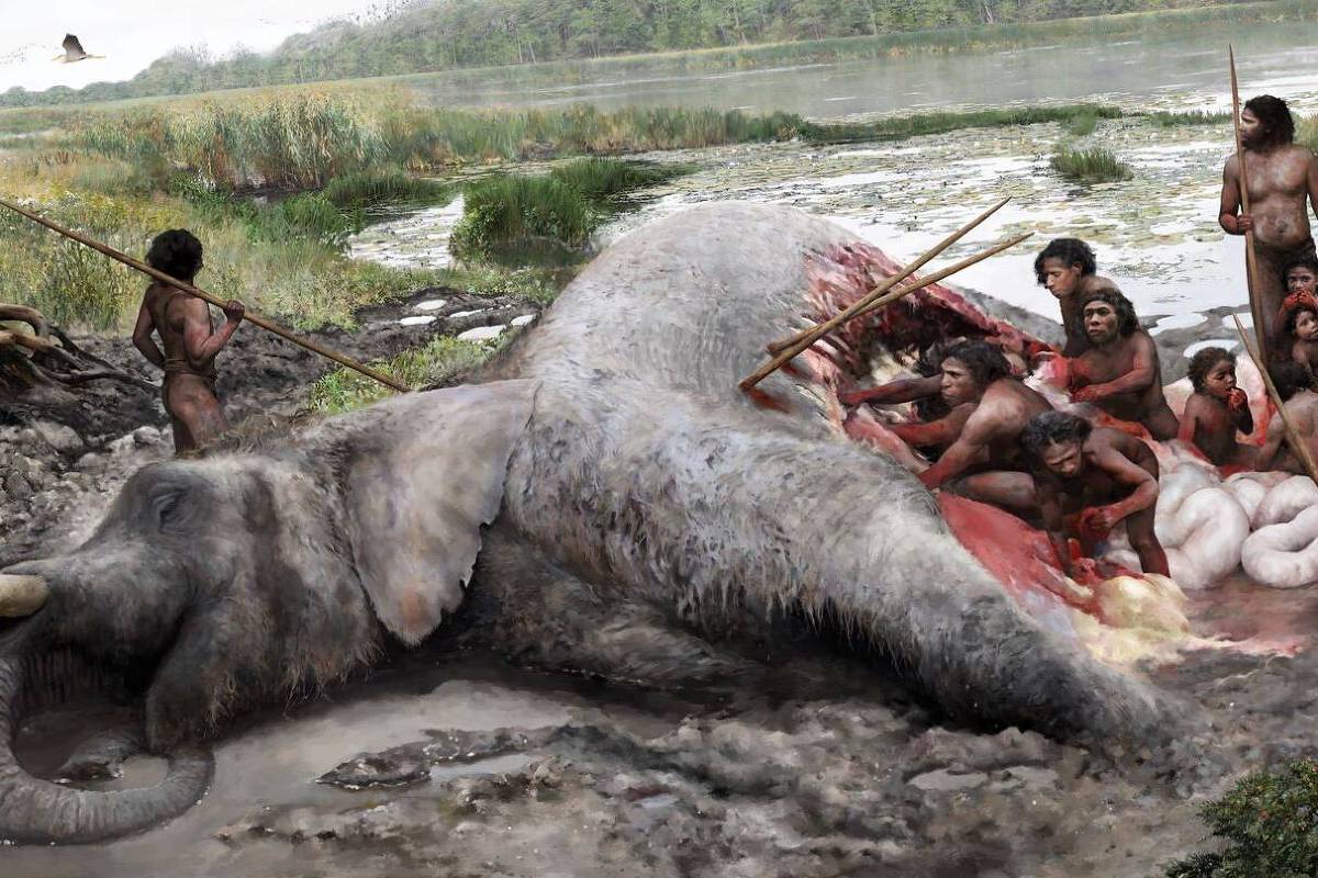 Grupo de pessoas pré-históricas, nuas e com lanças, ao redor de um mamute abatido em uma área pantanosa próxima a um rio. O mamute está deitado de lado, com ferimentos visíveis, enquanto os caçadores se aproximam para cortar a carne.