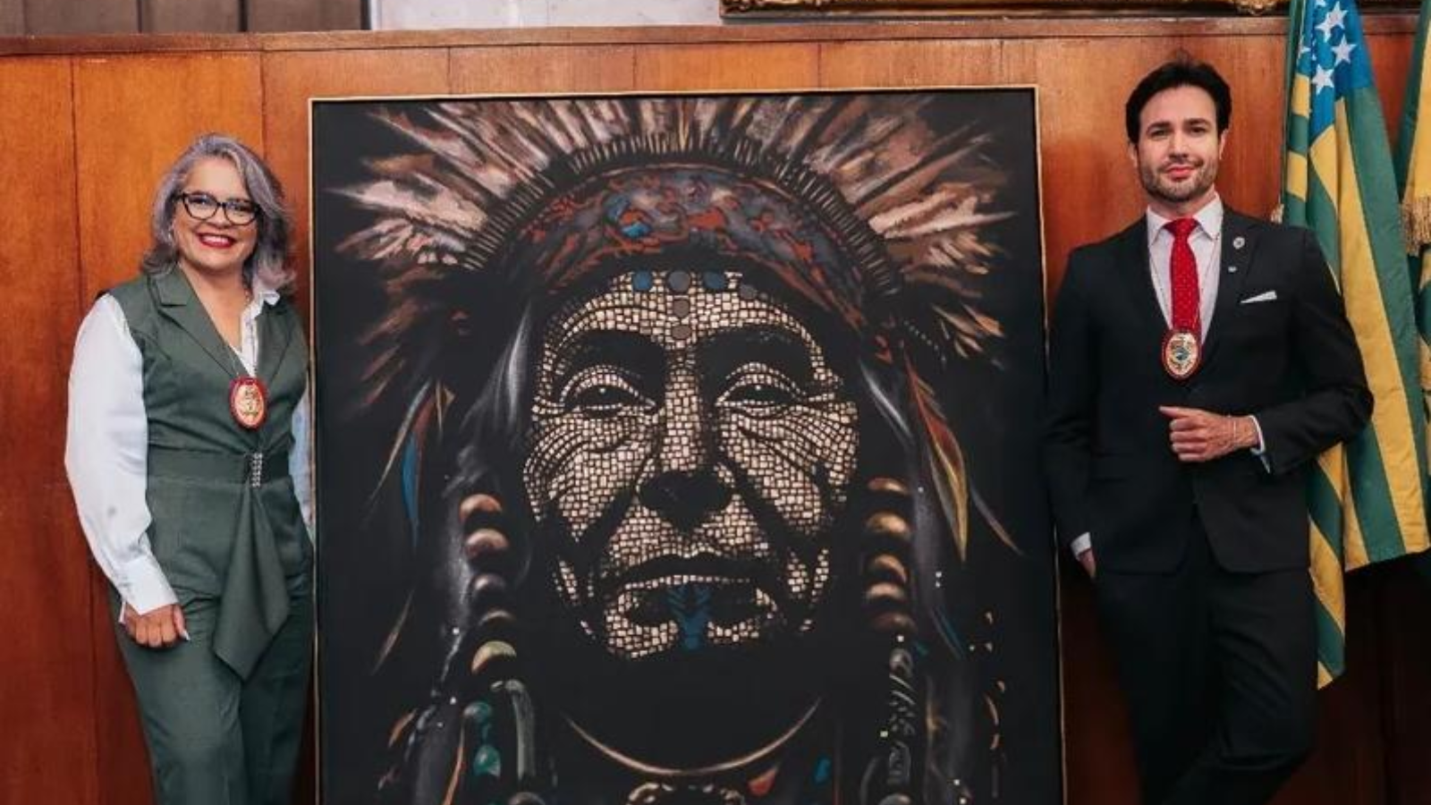 Paulo Ricardo Campos e Elisângela Dias posam ao lado de obra artística com referência indígena em ambiente institucional