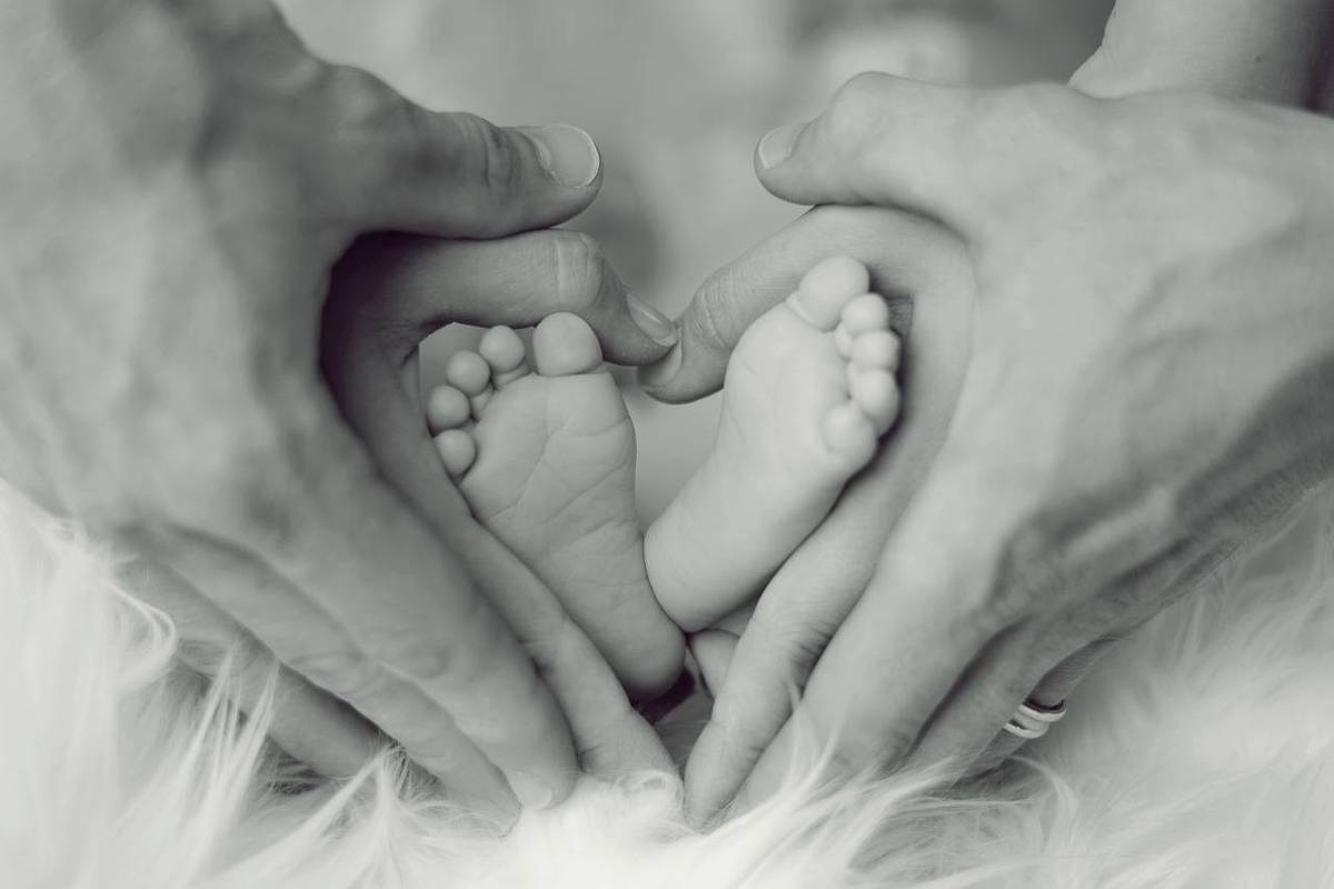 Pai e mãe usam as mãos em volta dos pés de um bebê para fazer um coração