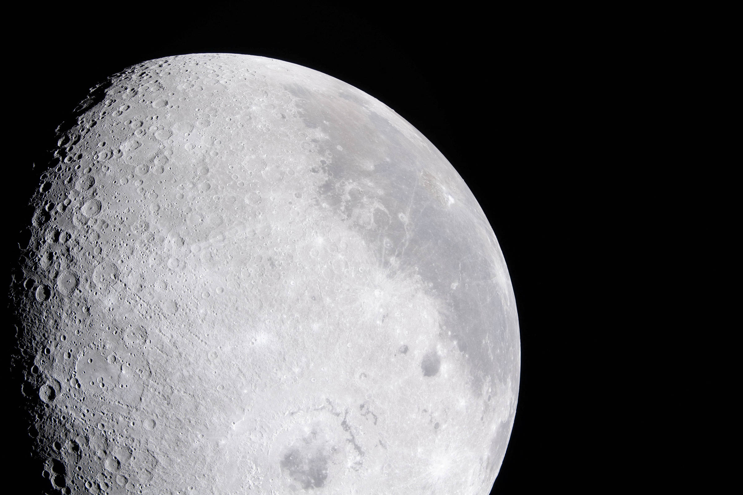 Imagem detalhada da superfície da Lua mostrando crateras e relevo em sua região iluminada contra fundo preto do espaço.