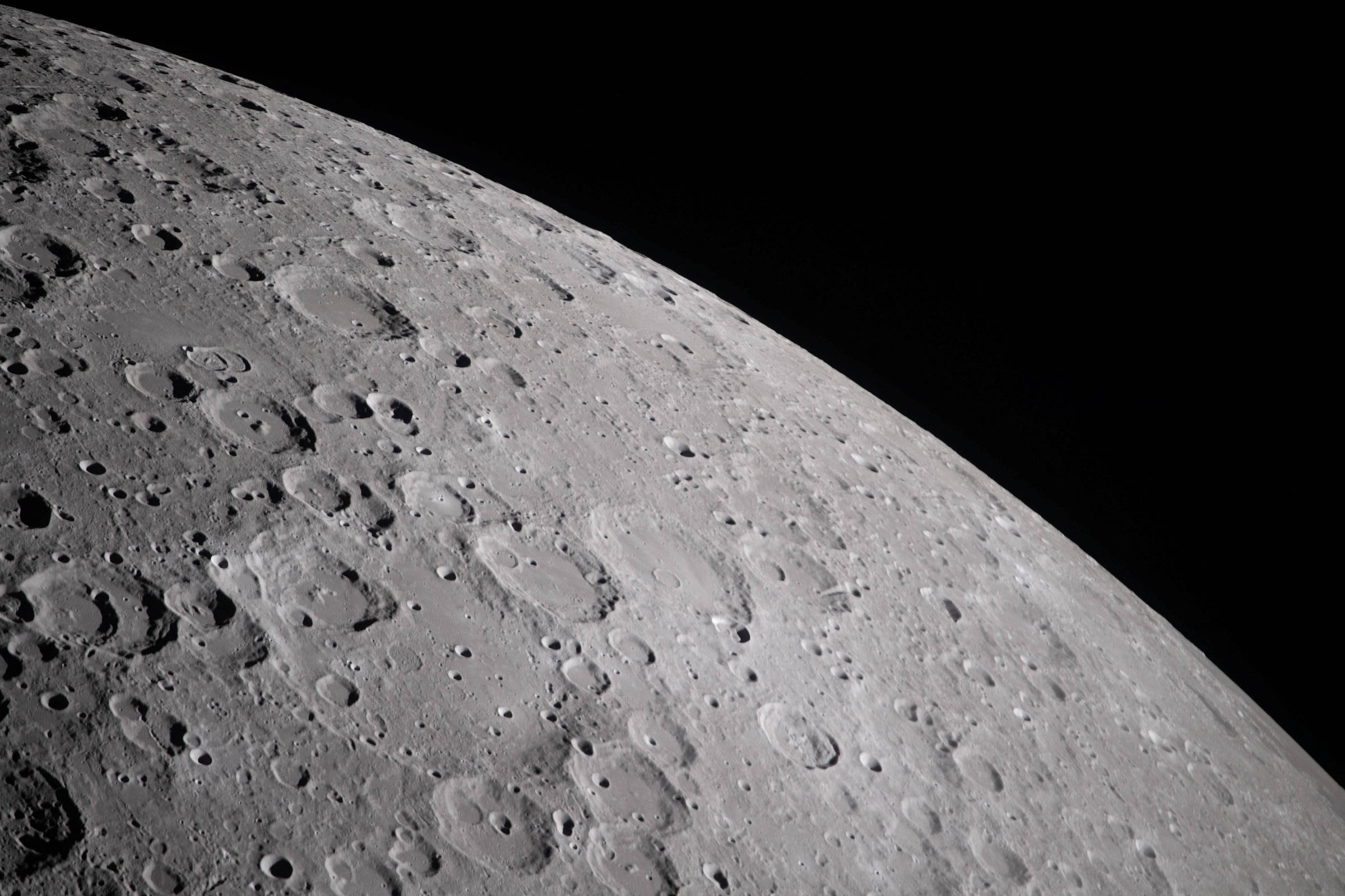 Vista detalhada da superfície da Lua mostrando numerosas crateras de diferentes tamanhos sob iluminação que destaca suas texturas. Fundo preto do espaço.