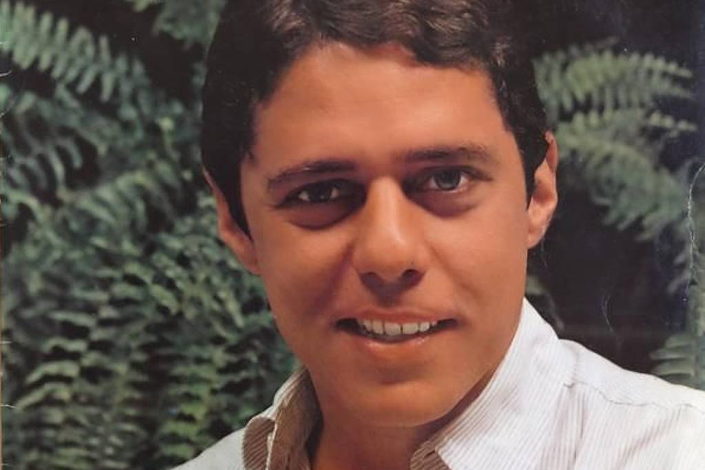 Chico Buarque aparece em close, sorrindo levemente, com camisa branca de gola aberta. Fundo com folhagens verdes desfocadas.