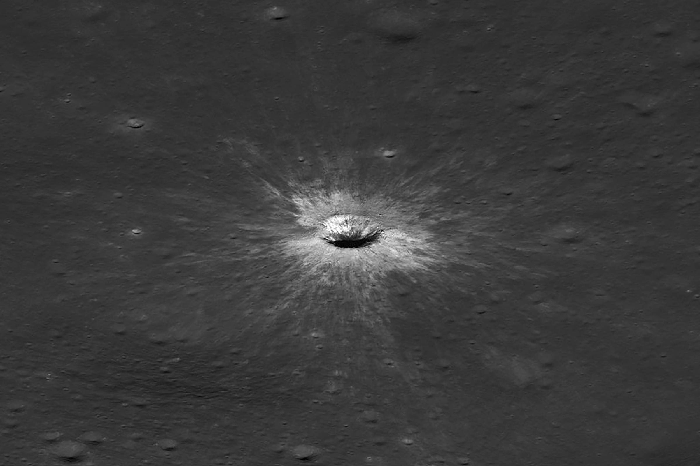 Cratera circular na superfície da Lua com raios claros irradiando ao redor, destacando-se em meio ao terreno escuro e acidentado.