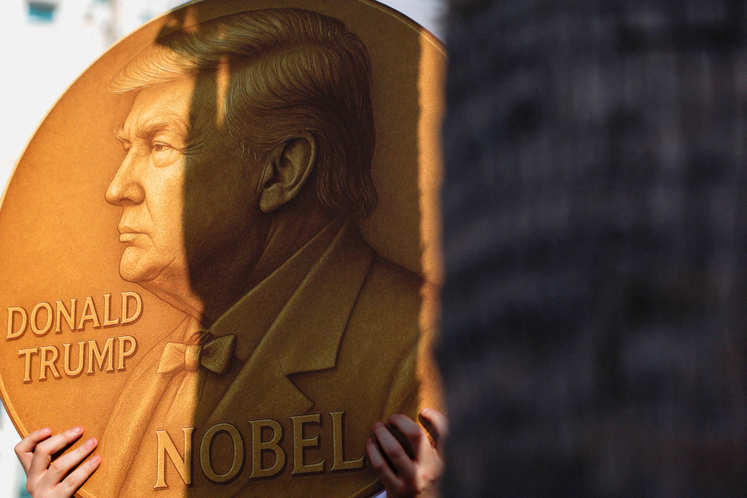 Medalha dourada gigante com relevo do perfil de Donald Trump e as palavras